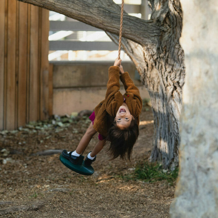 Child Smiles as she looks upside down on an outdoor swing
